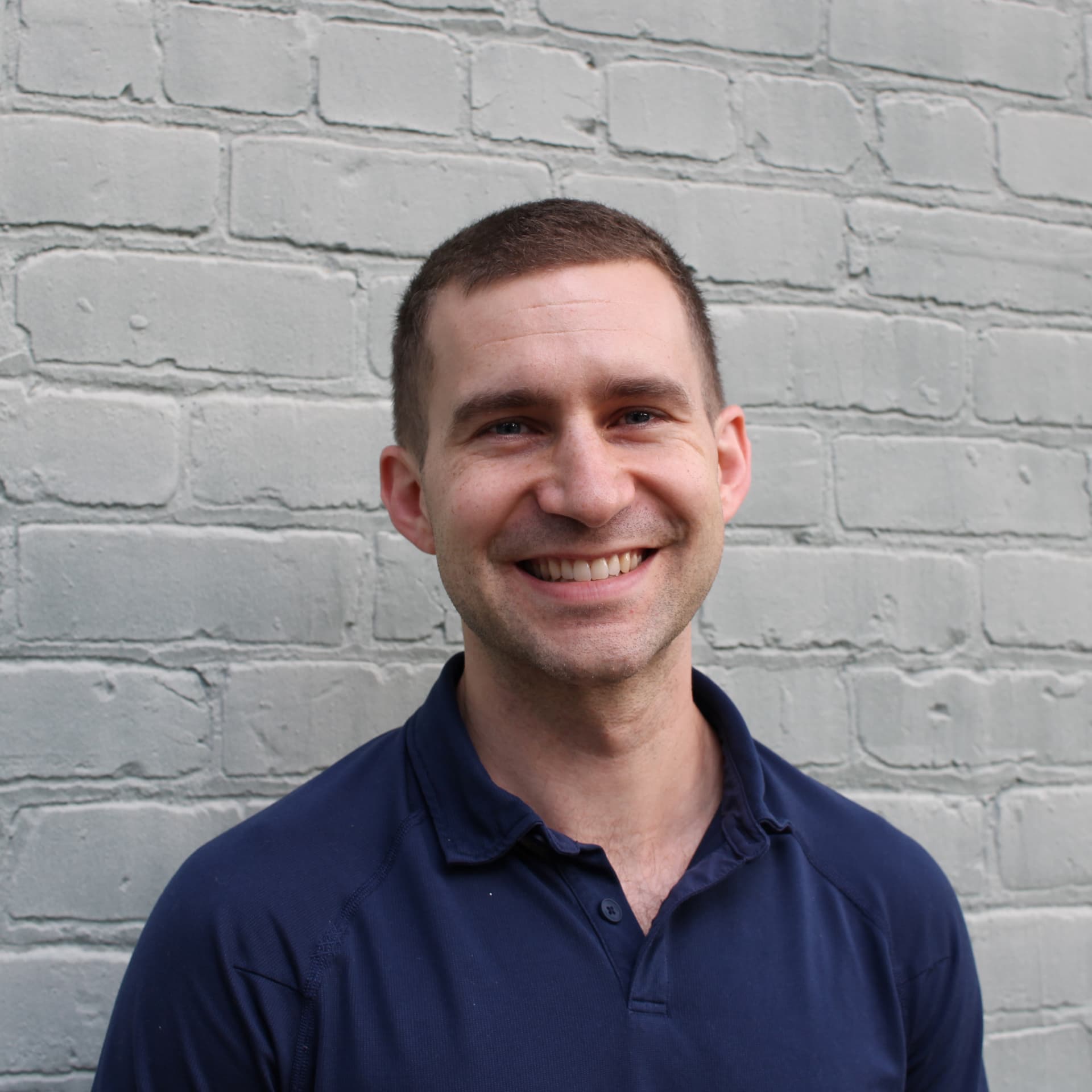 Smiling headshot in front of a painted grey brick wall