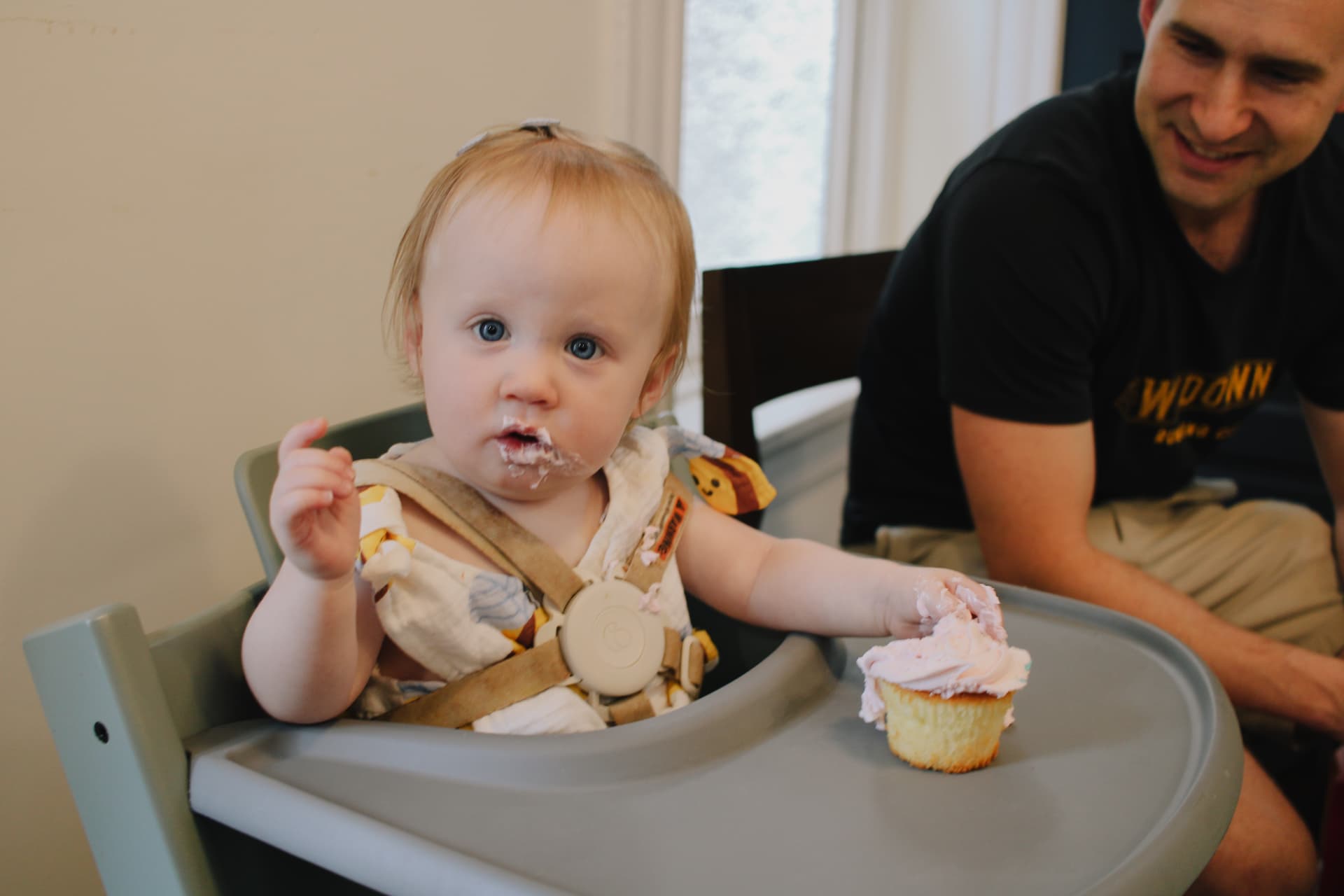 Phoebe in her highchair with a pink frosted cupcake
