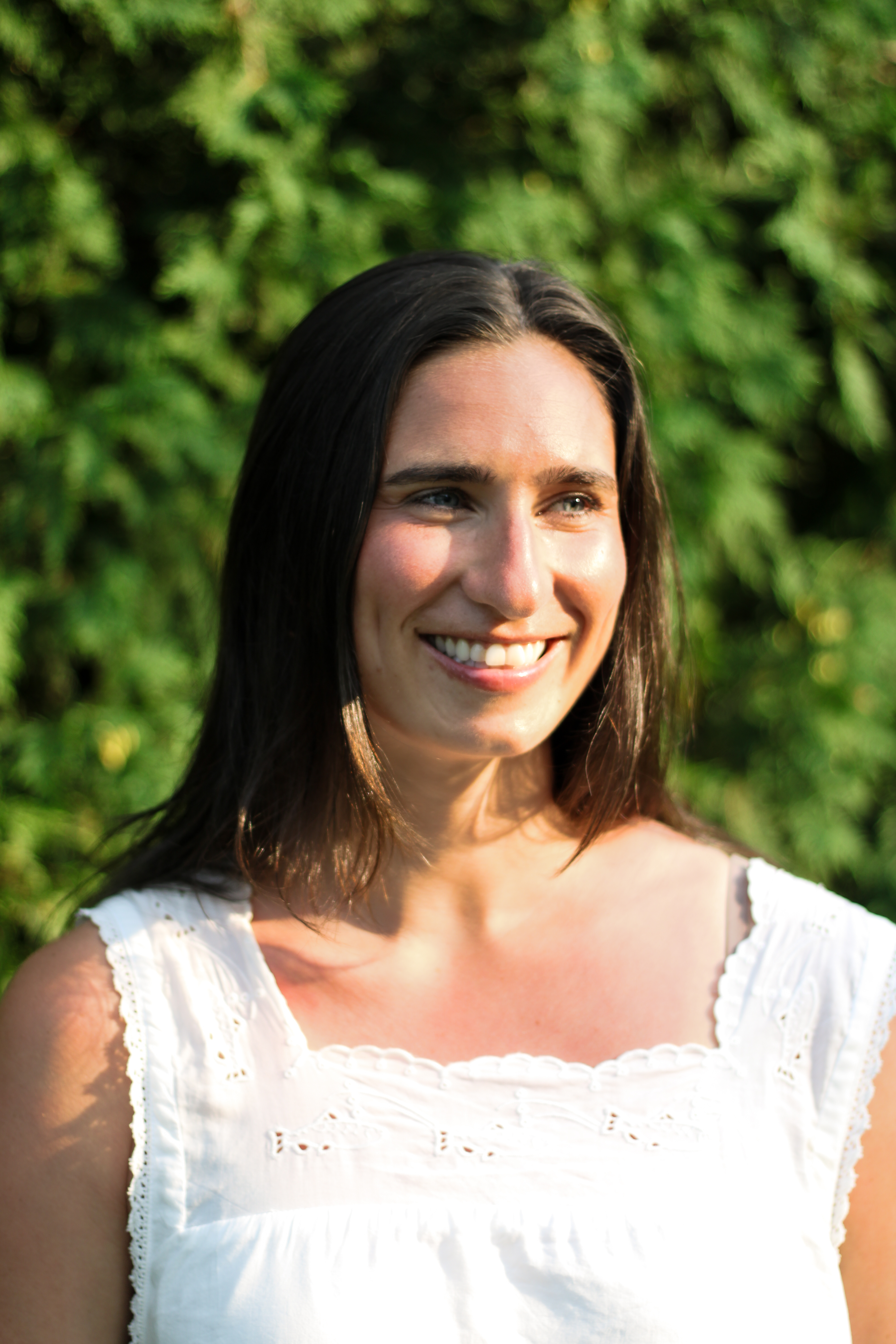 Sarah smiling in a white dress in front of a green hedge