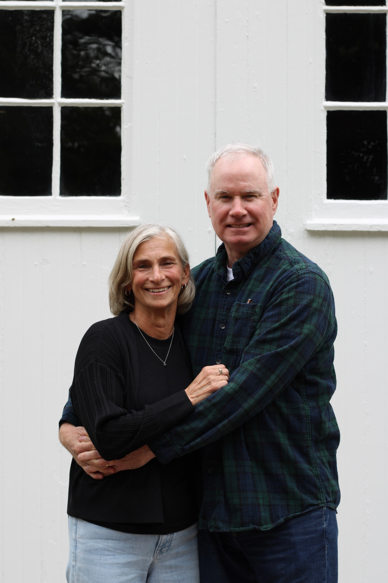 Jim and Sue smiling together in front of white barn doors