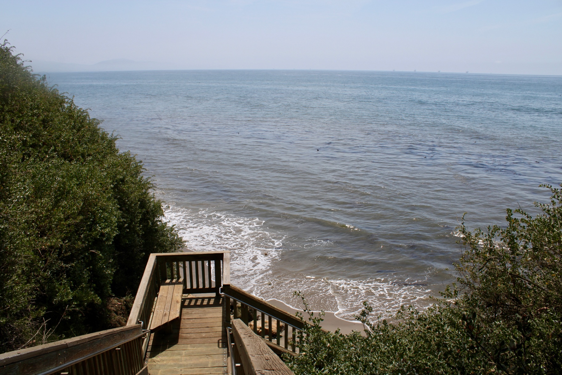 Wooden boardwalk leading down through coastal scrub to the Santa Barbara shore
