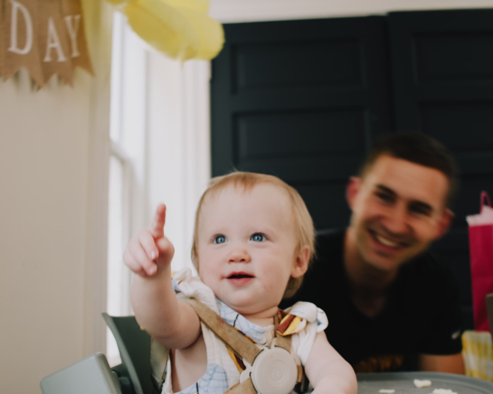Phoebe pointing from her highchair with a Happy Bee Day banner behind her