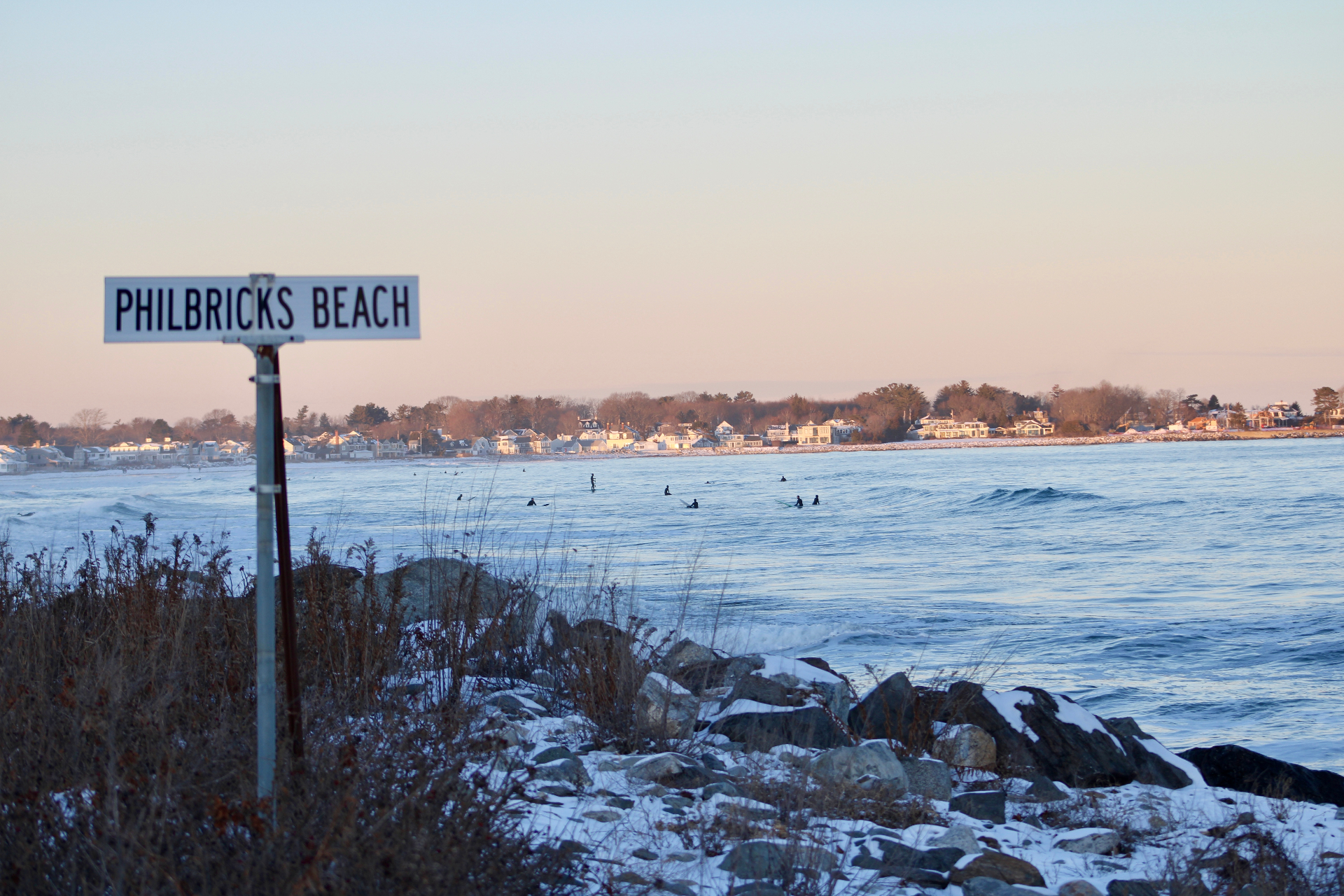 Philbricks Beach sign at Rye, New Hampshire with surfers in the Atlantic surf