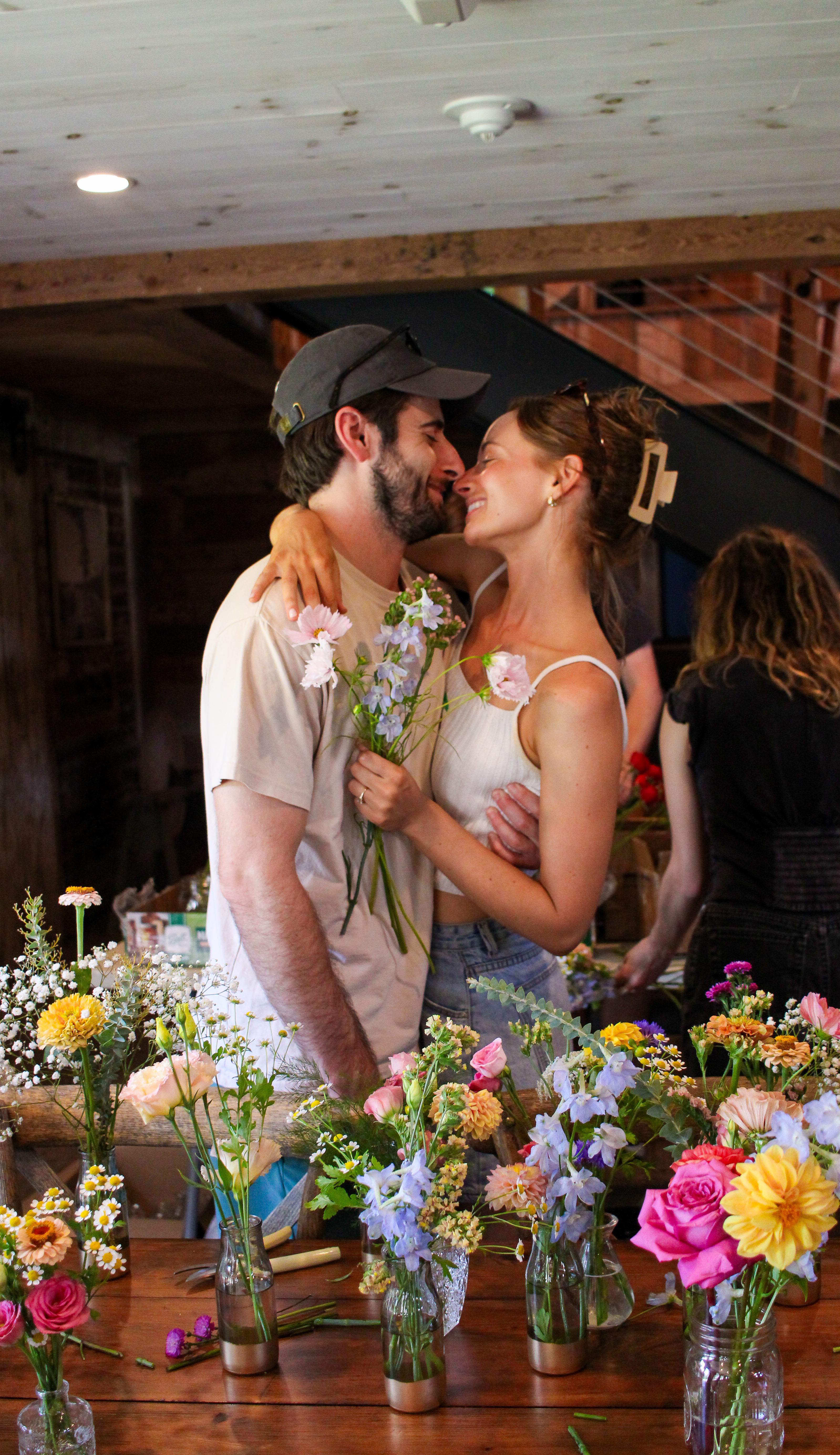 Caroline and Jamie kissing behind a table of floral arrangements