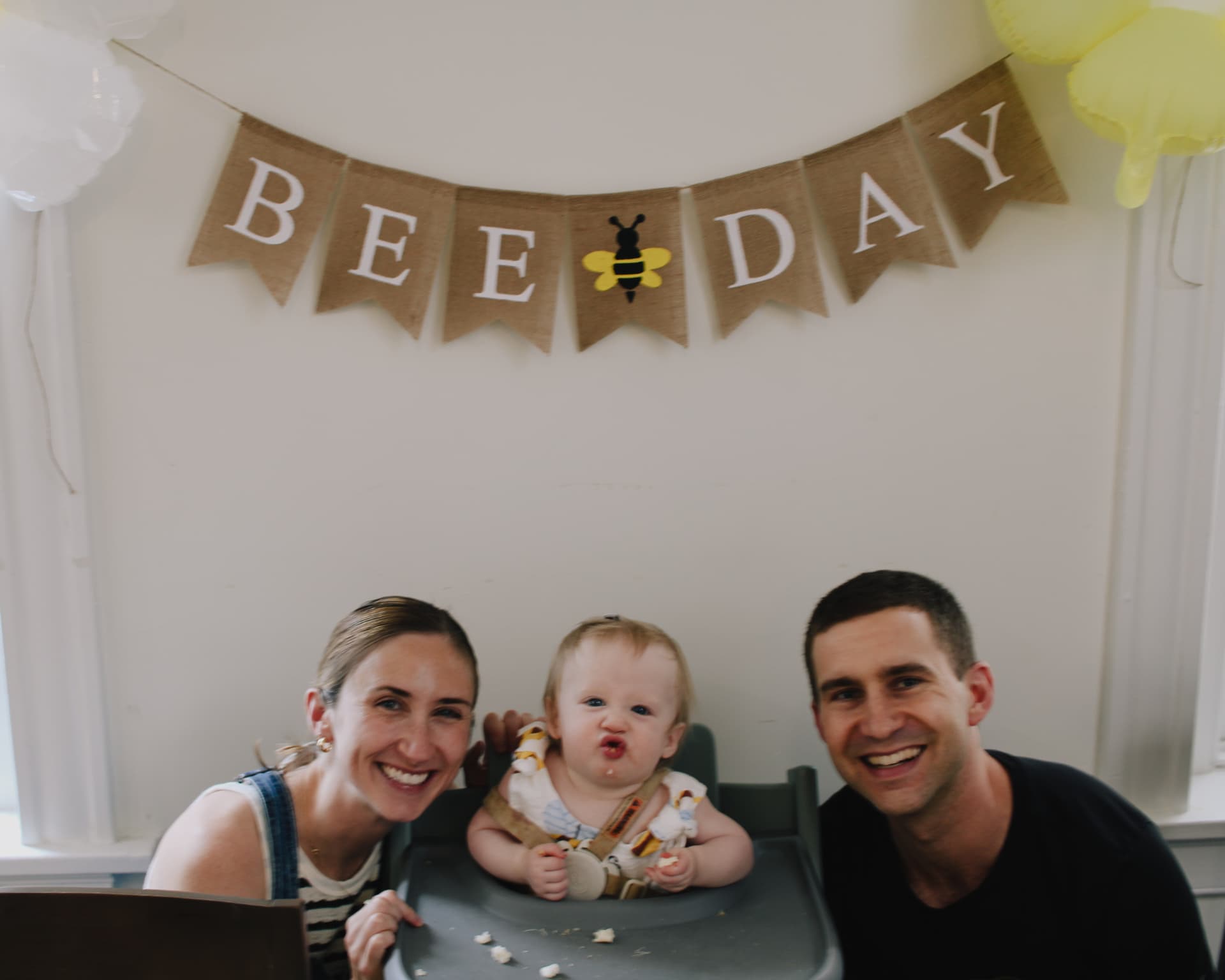 Phoebe with her parents under the Happy Bee Day banner