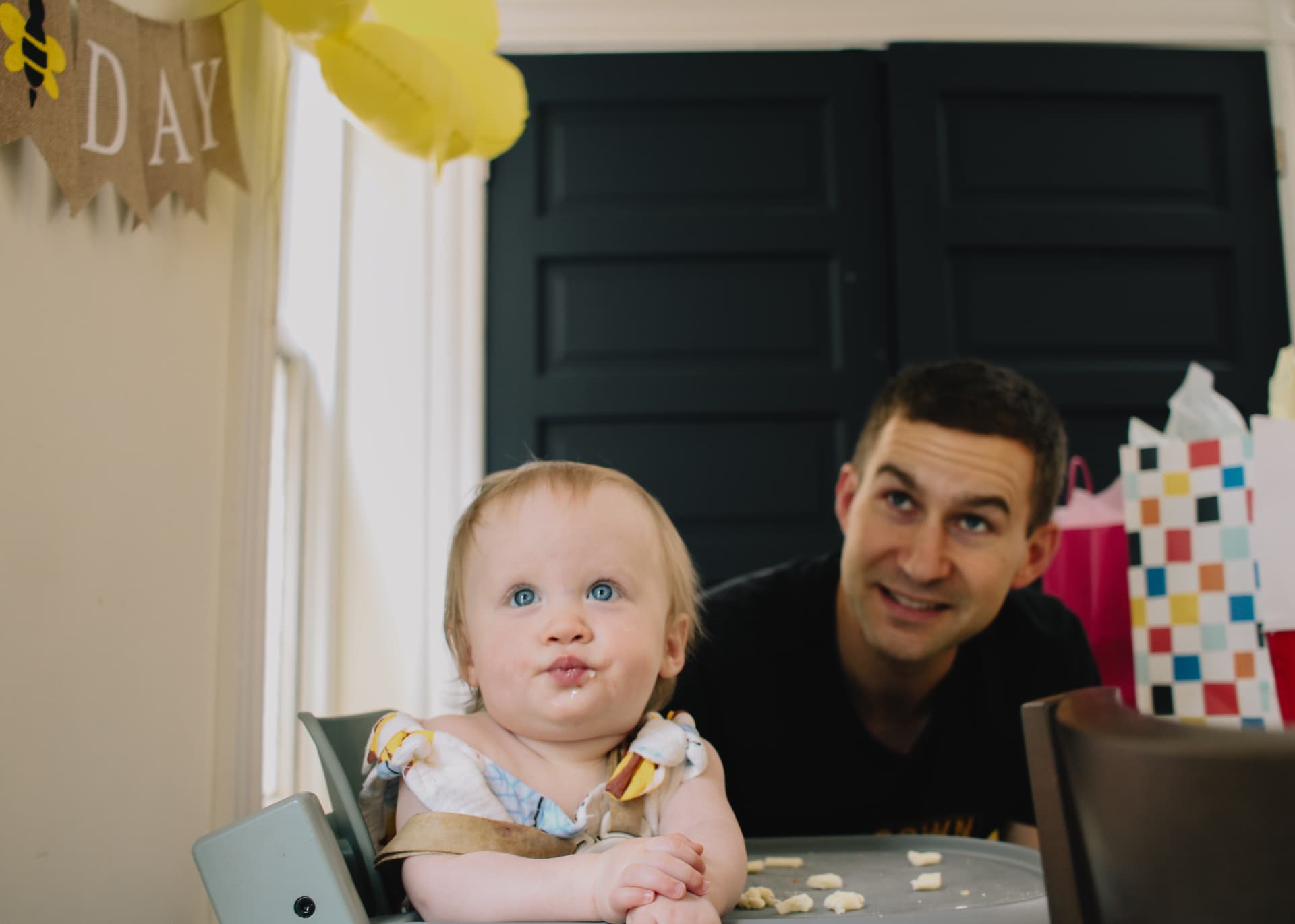 Phoebe in her highchair with her dad under the Happy Bee Day banner