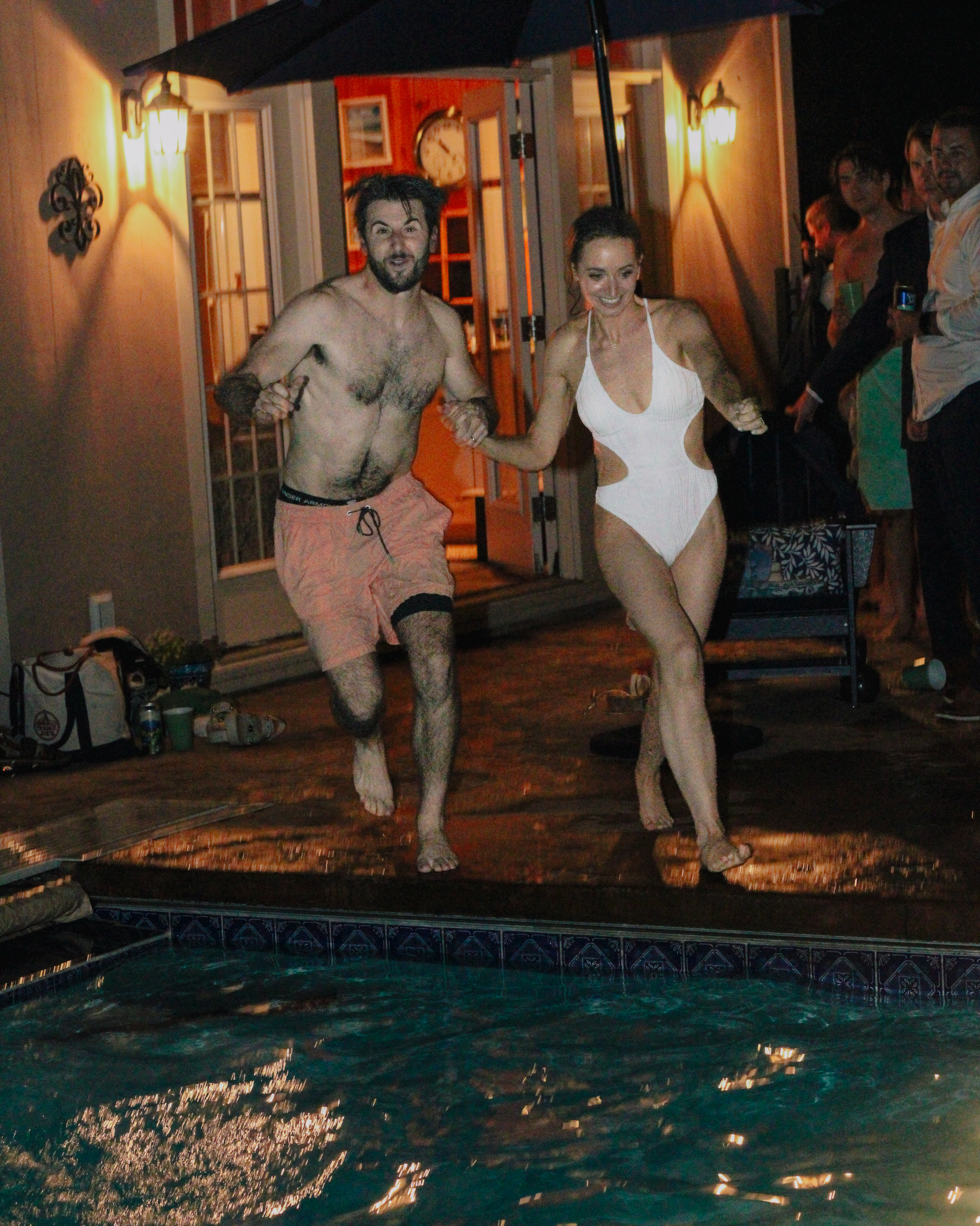 Caroline and Jamie holding hands as they run and jump into the pool at night