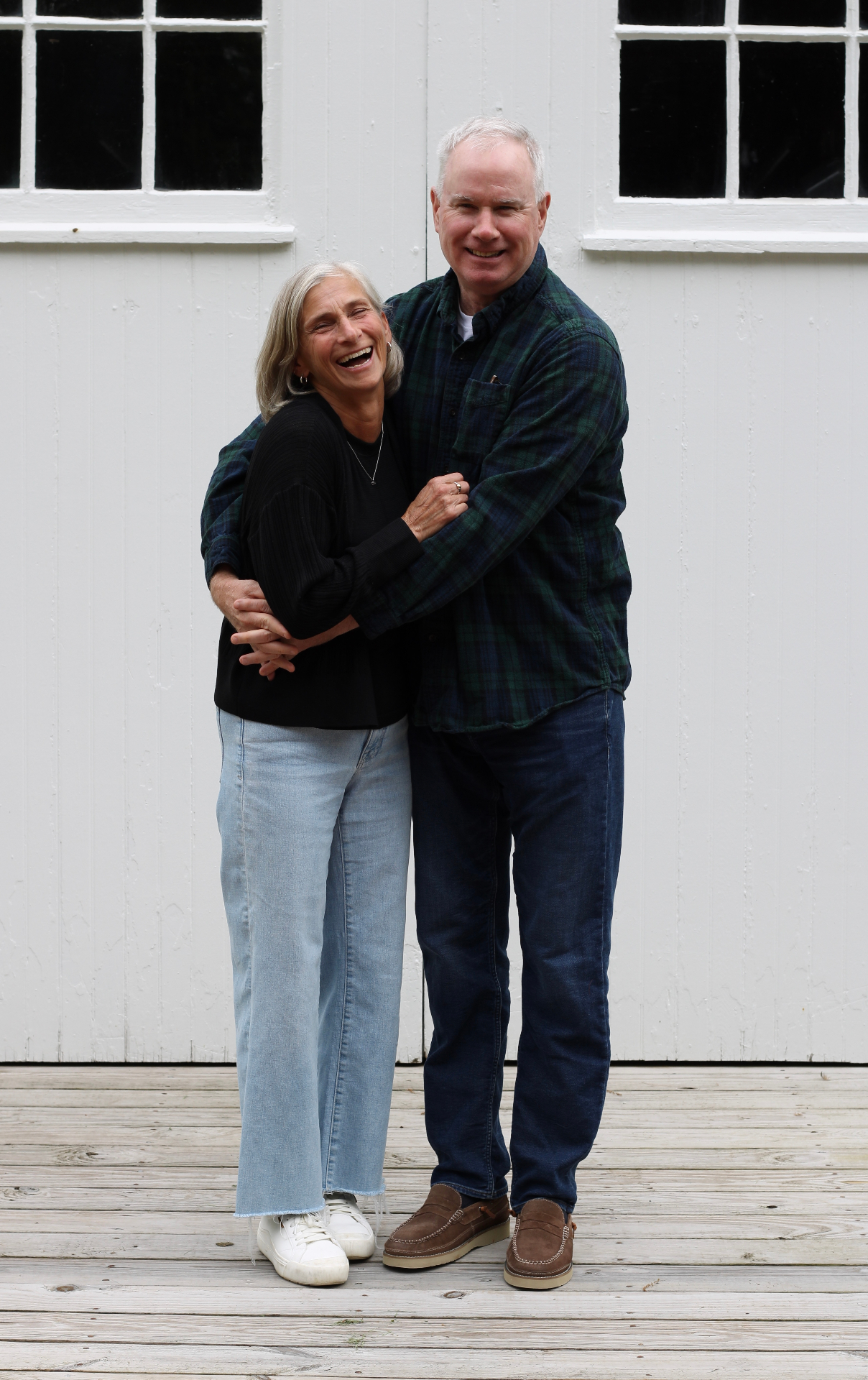 Jim and Sue laughing in an embrace in front of a white barn
