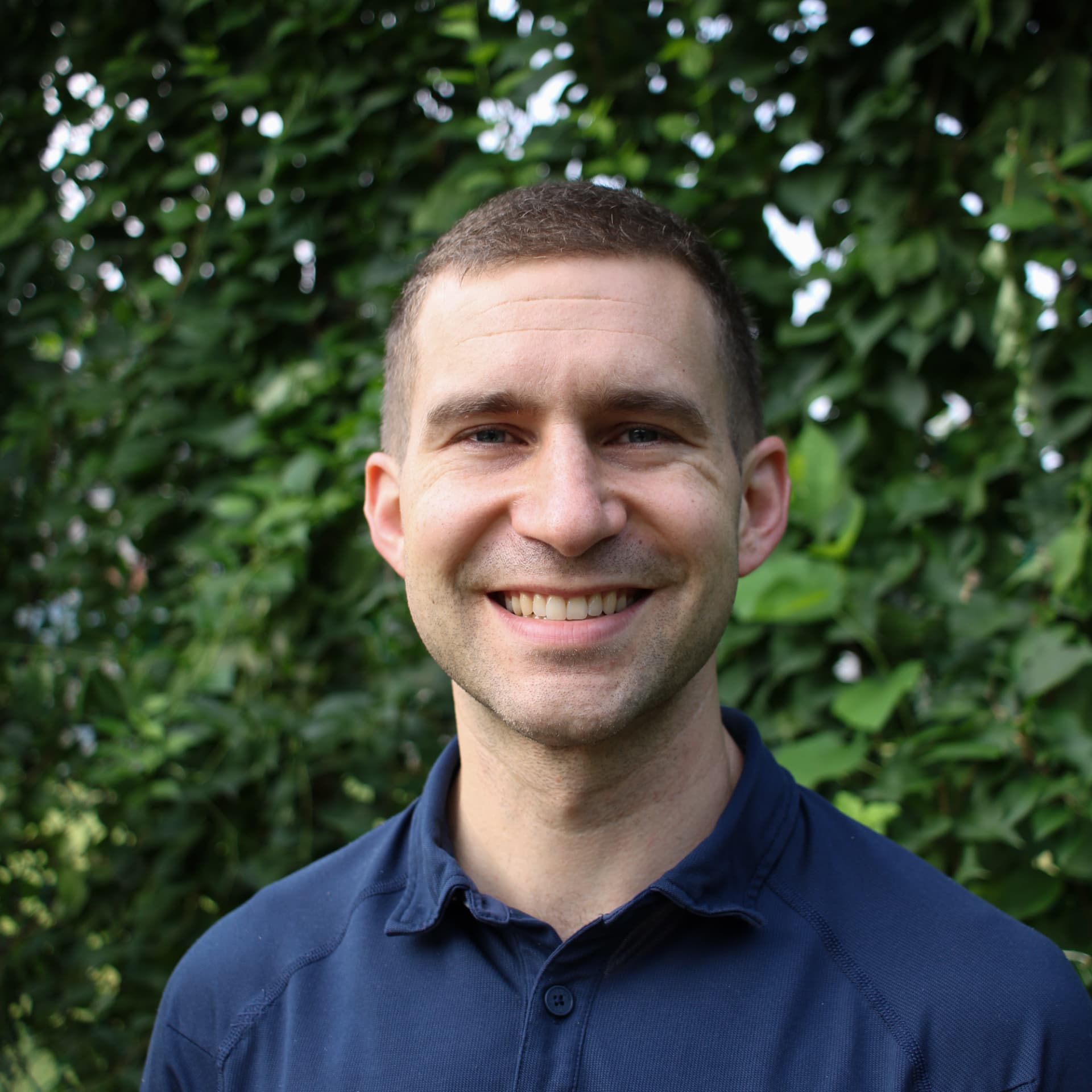 Smiling headshot in a navy polo in front of a green ivy wall