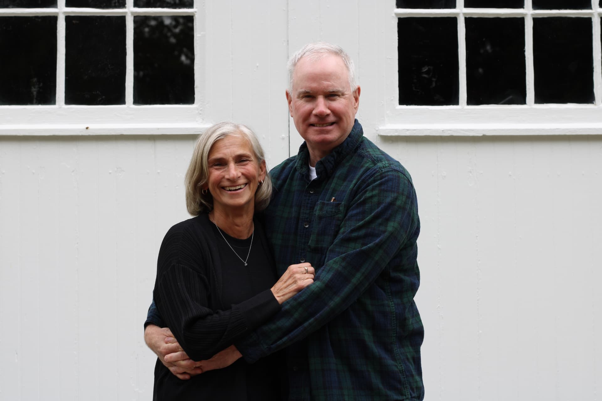 Jim and Sue smiling together in front of a white barn door