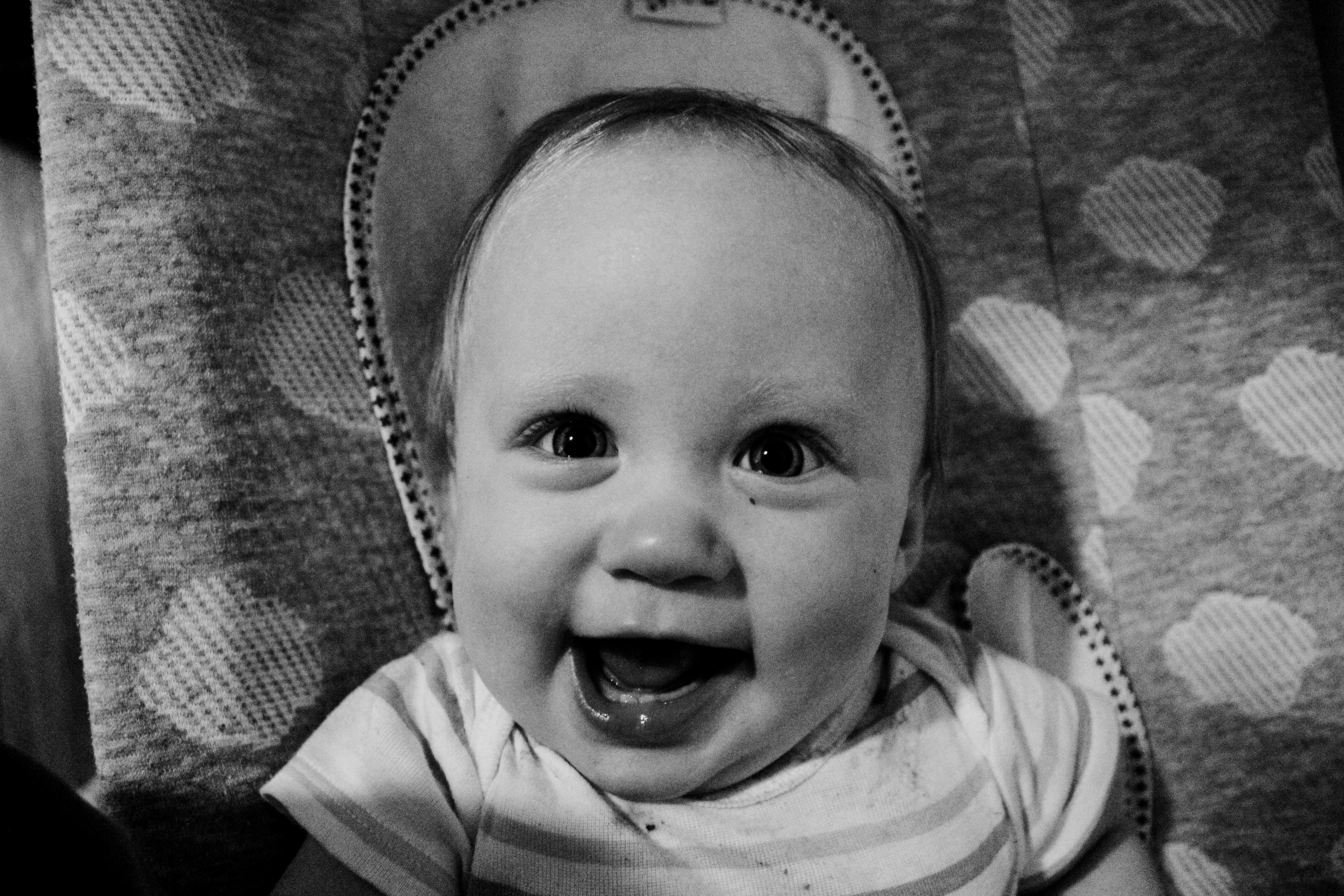 Black and white portrait of a smiling baby in a bouncer