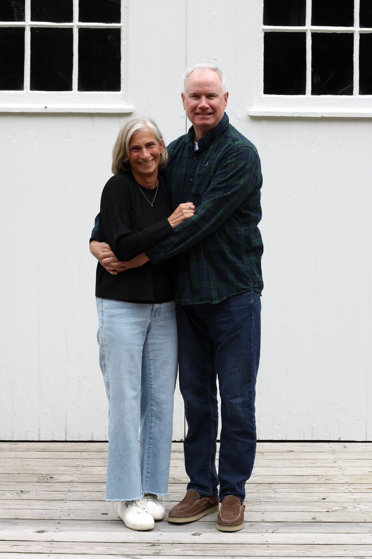 Jim and Sue holding each other in front of white barn doors