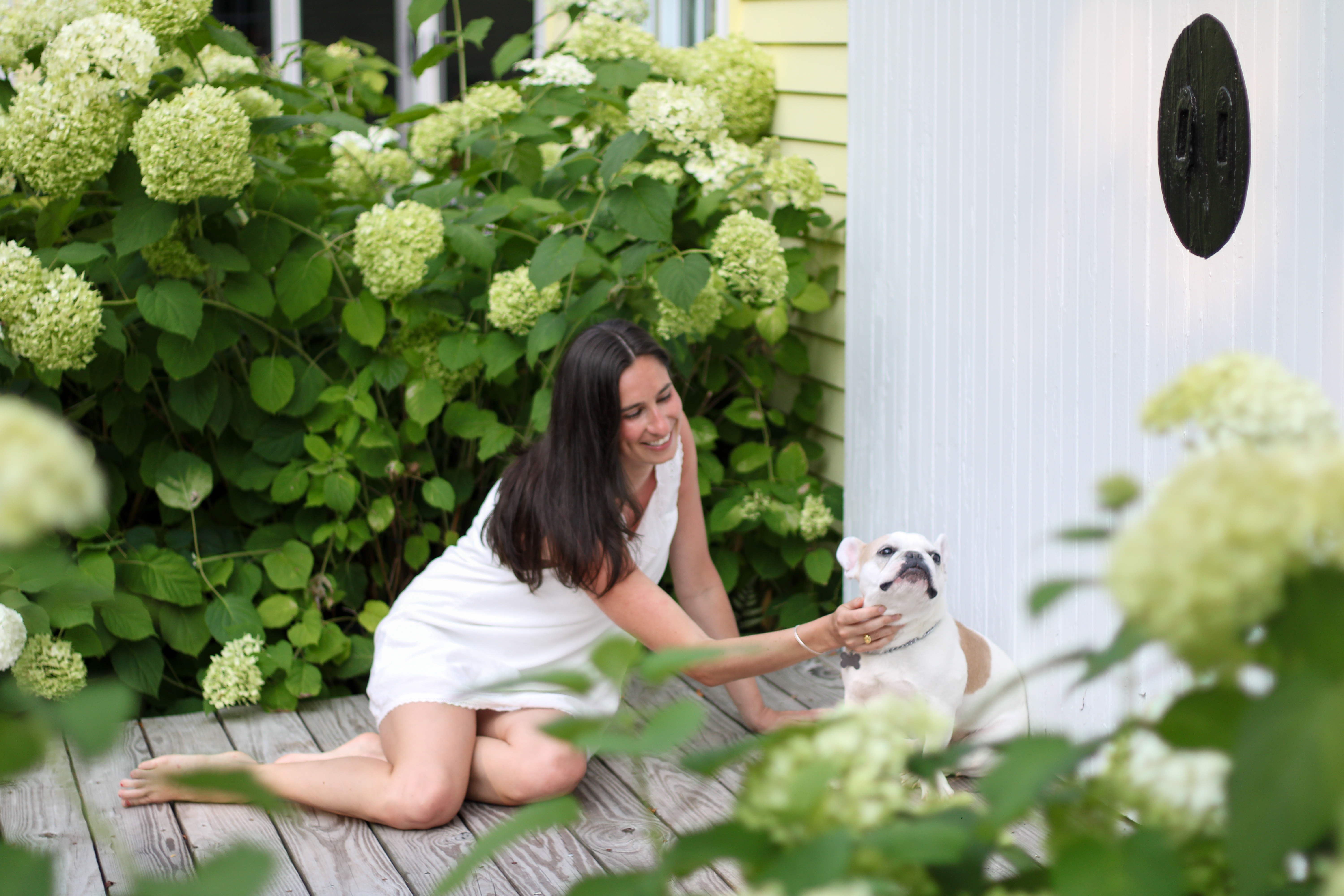 Sarah reaching toward her French bulldog on the porch