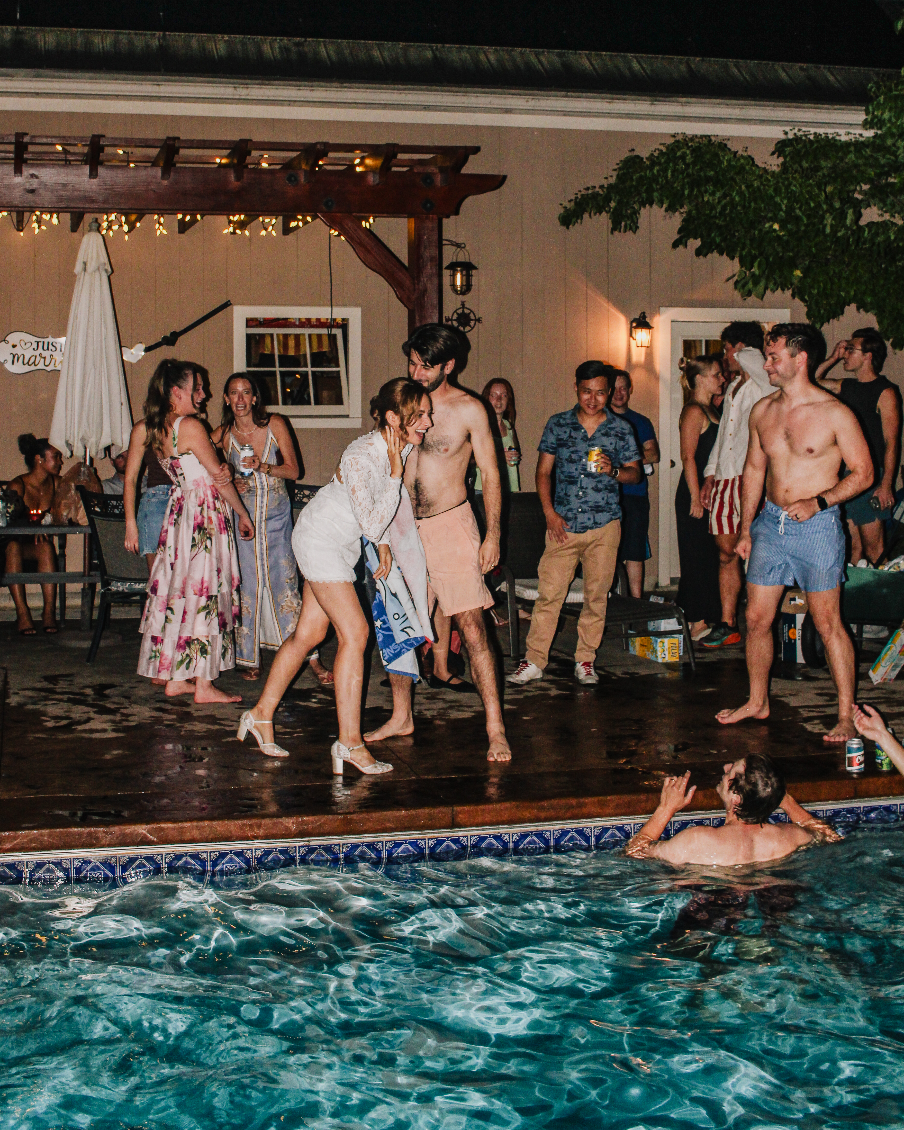 Caroline and Jamie laughing poolside with guests as someone swims nearby