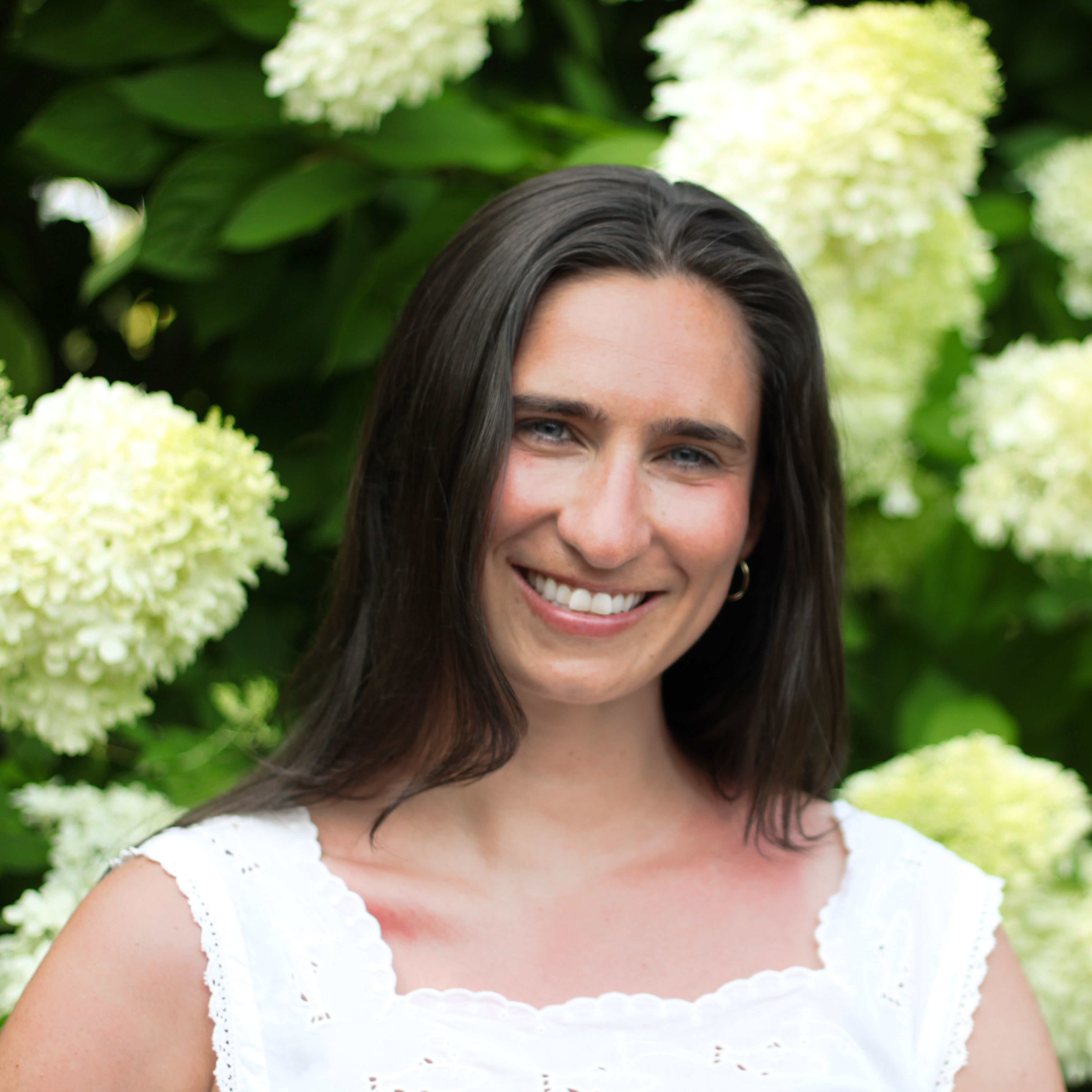 Close-up of Sarah smiling in front of white hydrangea blooms