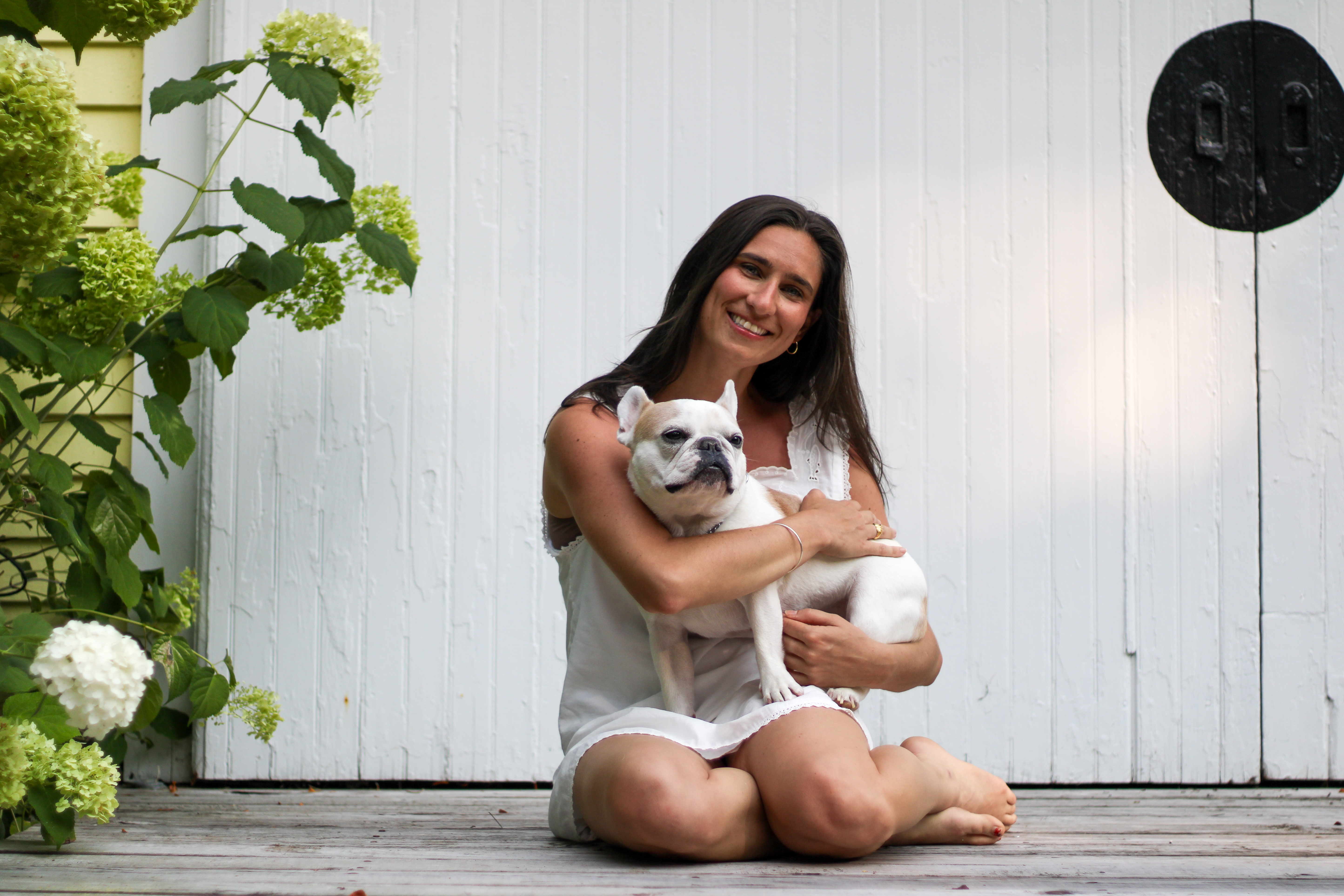 Sarah holding her French bulldog close beside white hydrangeas