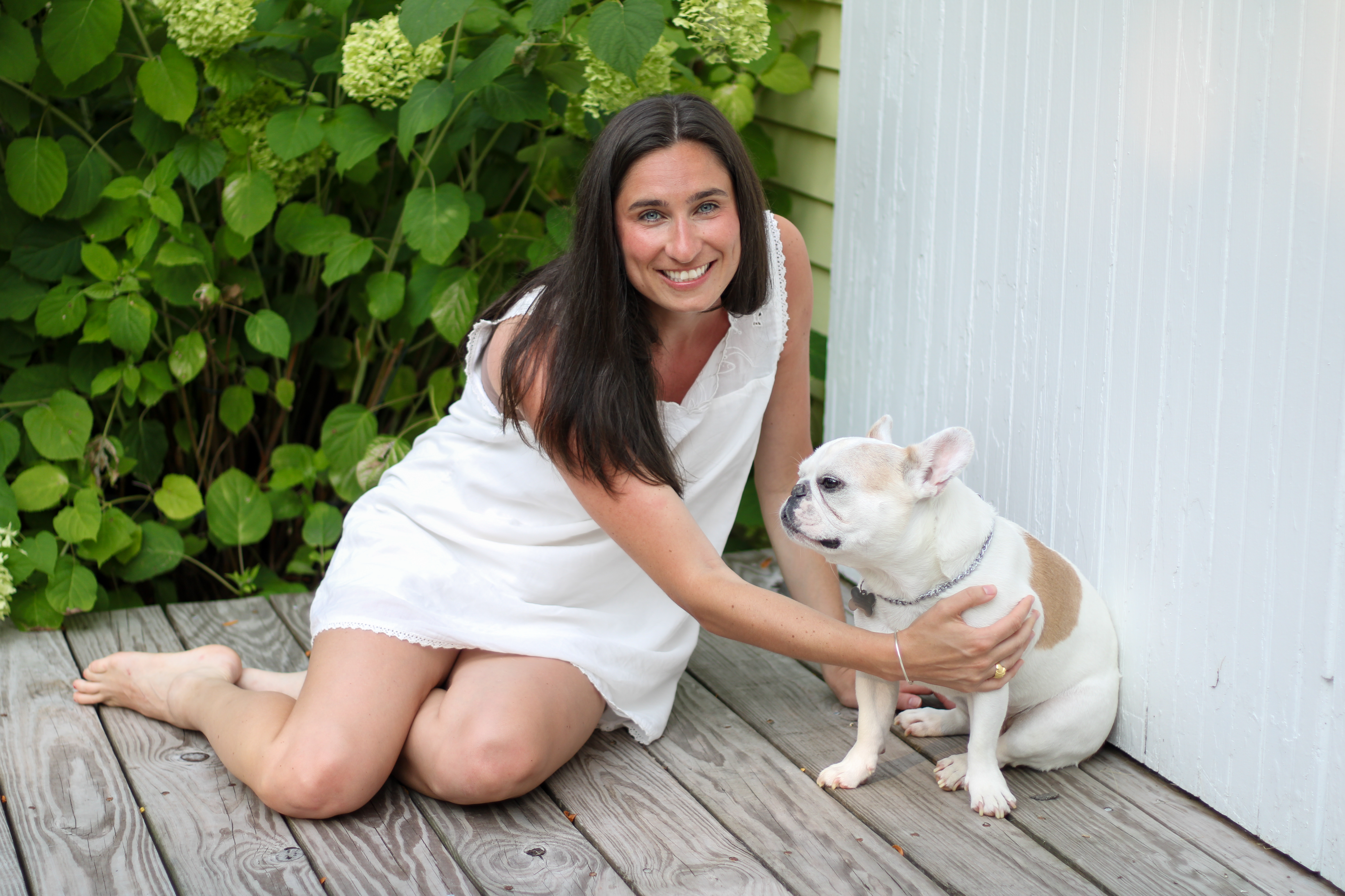 Sarah sitting on a porch with her French bulldog beside hydrangeas