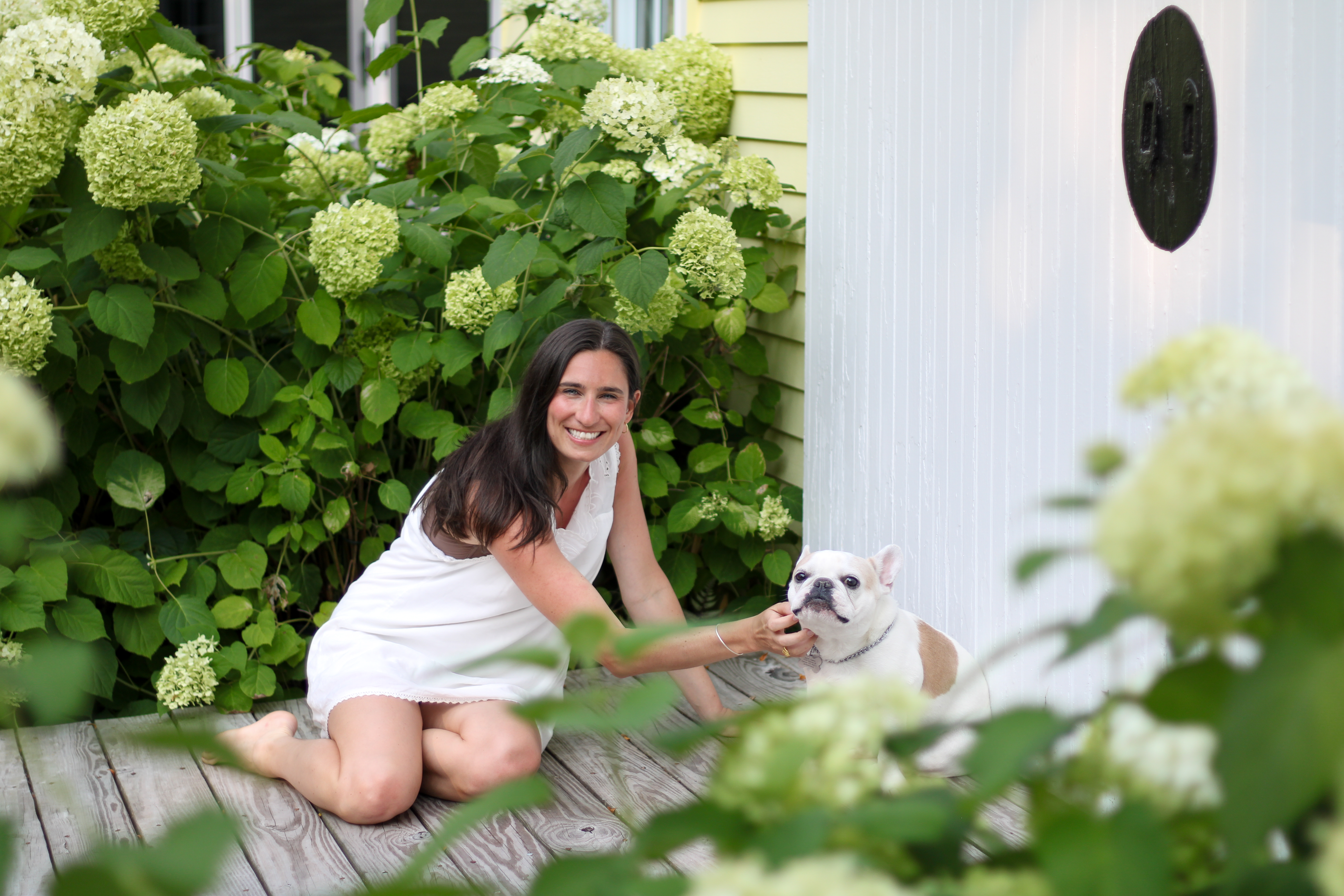 Sarah laughing with her French bulldog framed by hydrangea blooms
