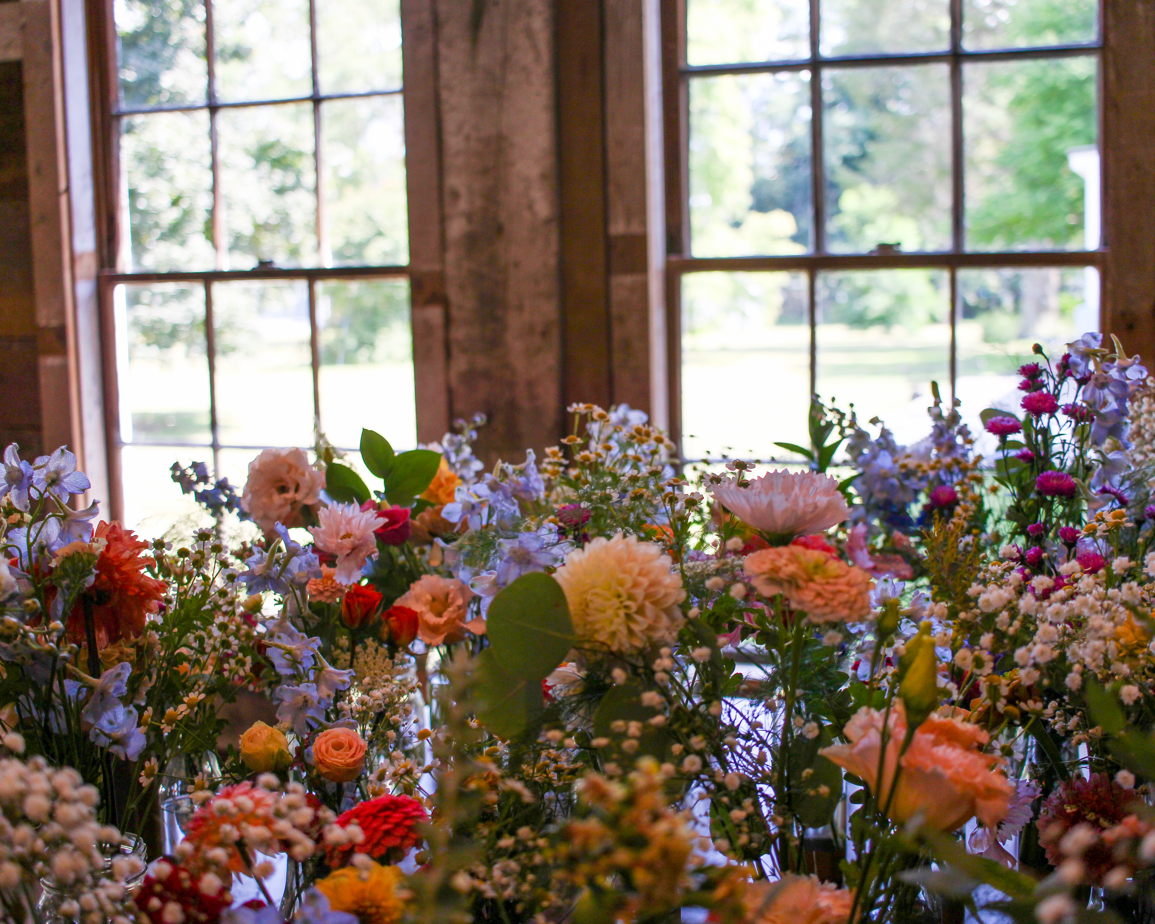Wildflower arrangements in bud vases backlit by tall barn windows
