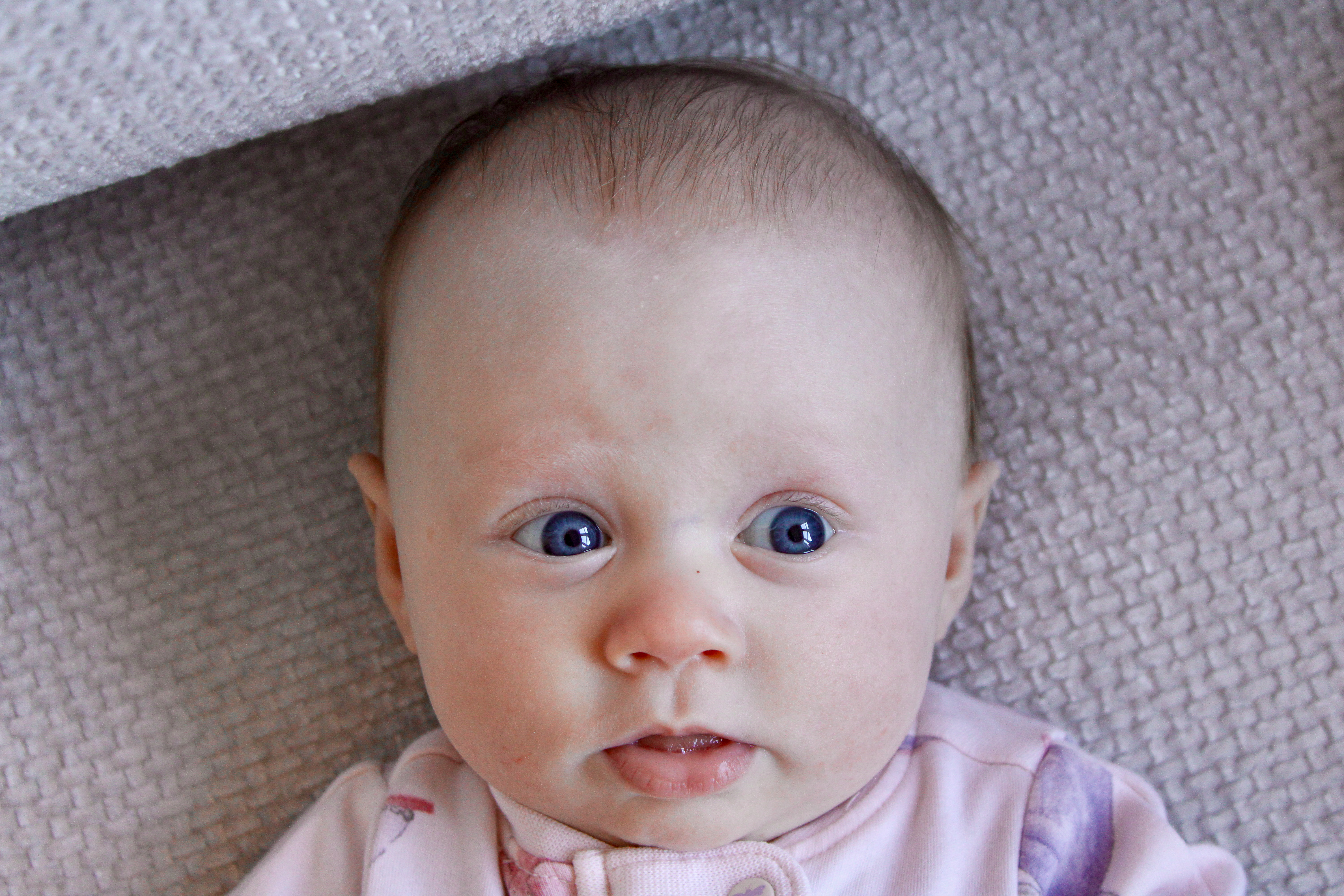 A baby with bright blue eyes looking up while lying on a light gray couch