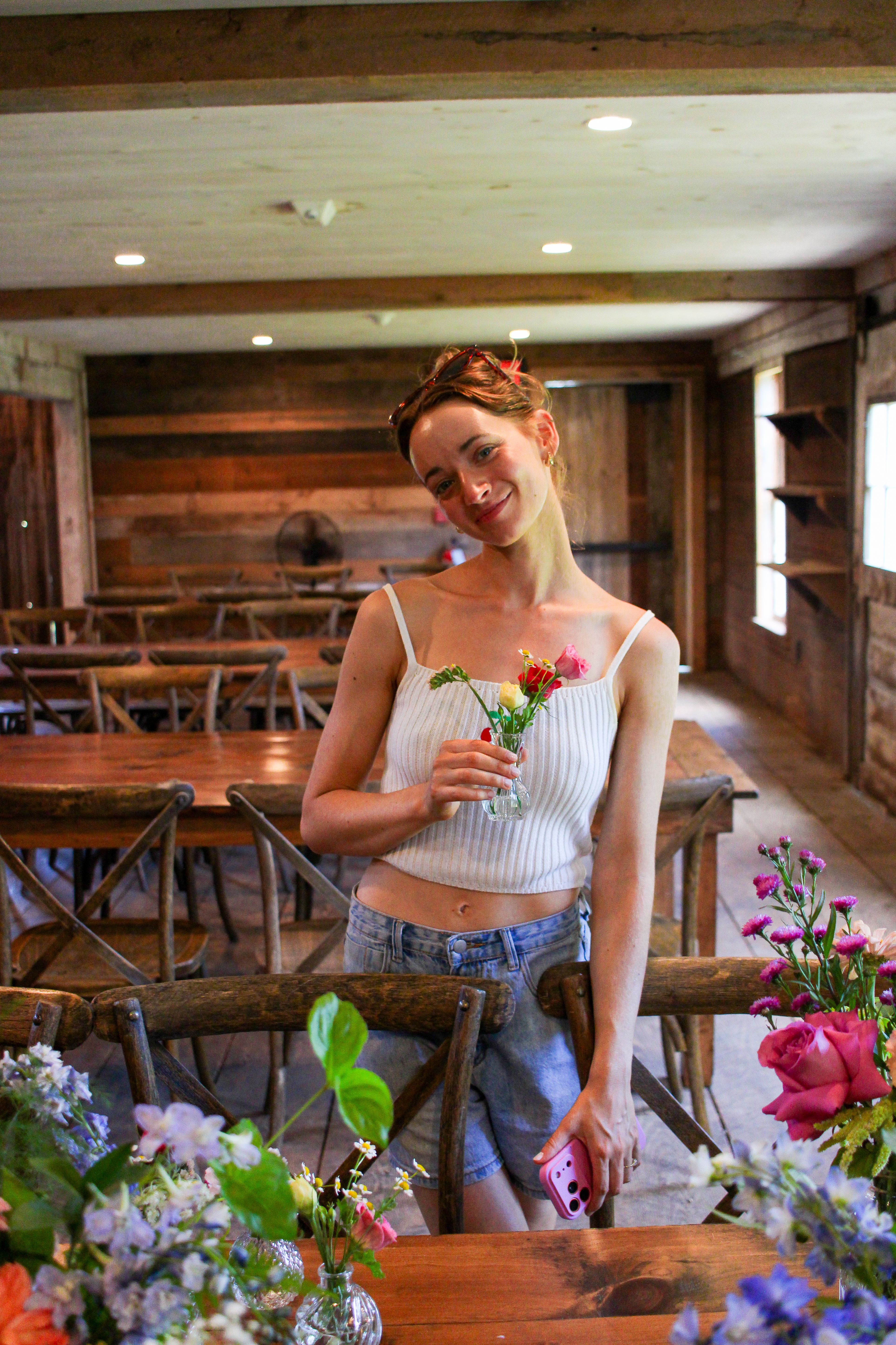 Caroline smiling as she holds a small bud vase of flowers in the barn