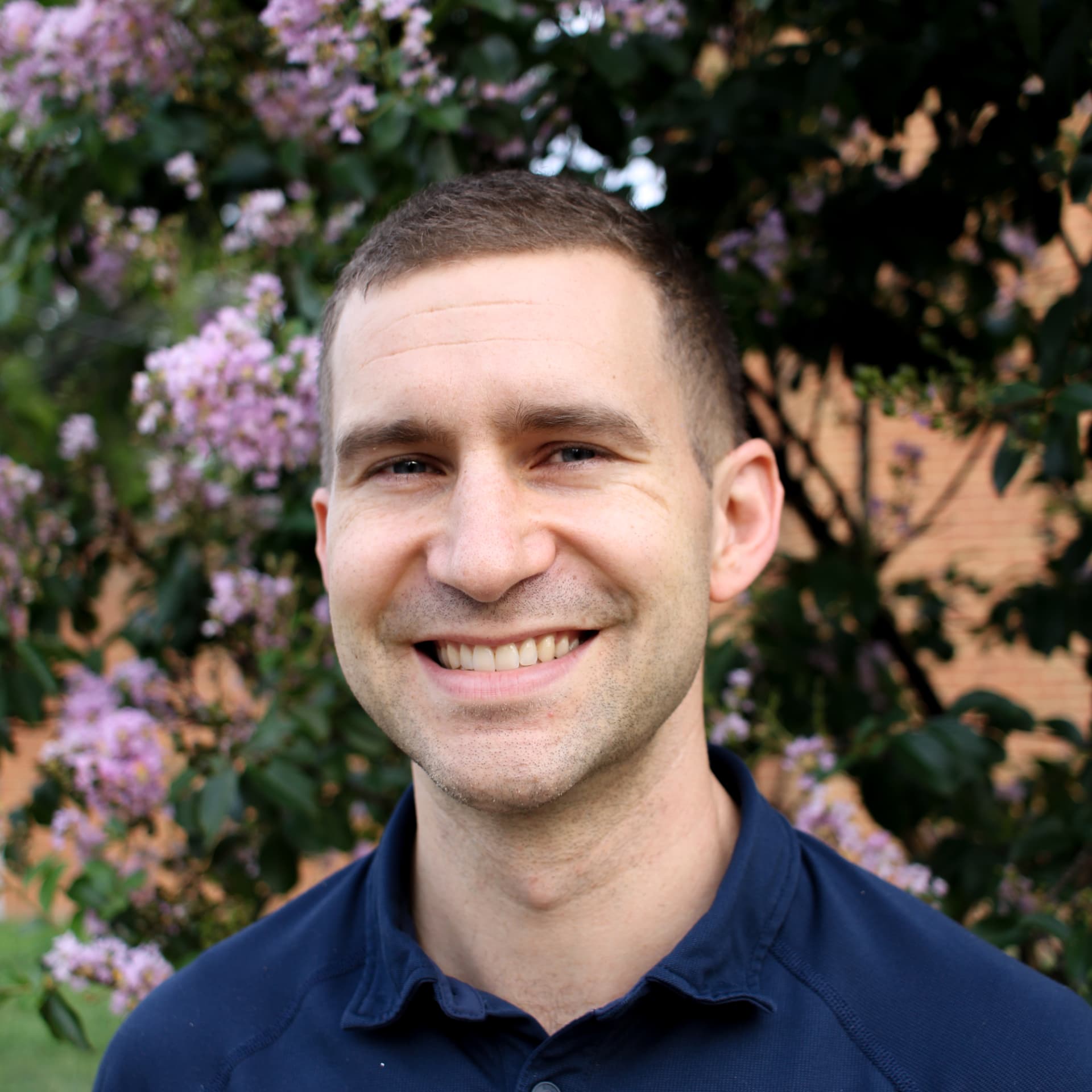 Smiling headshot in a navy polo in front of a flowering ivy wall