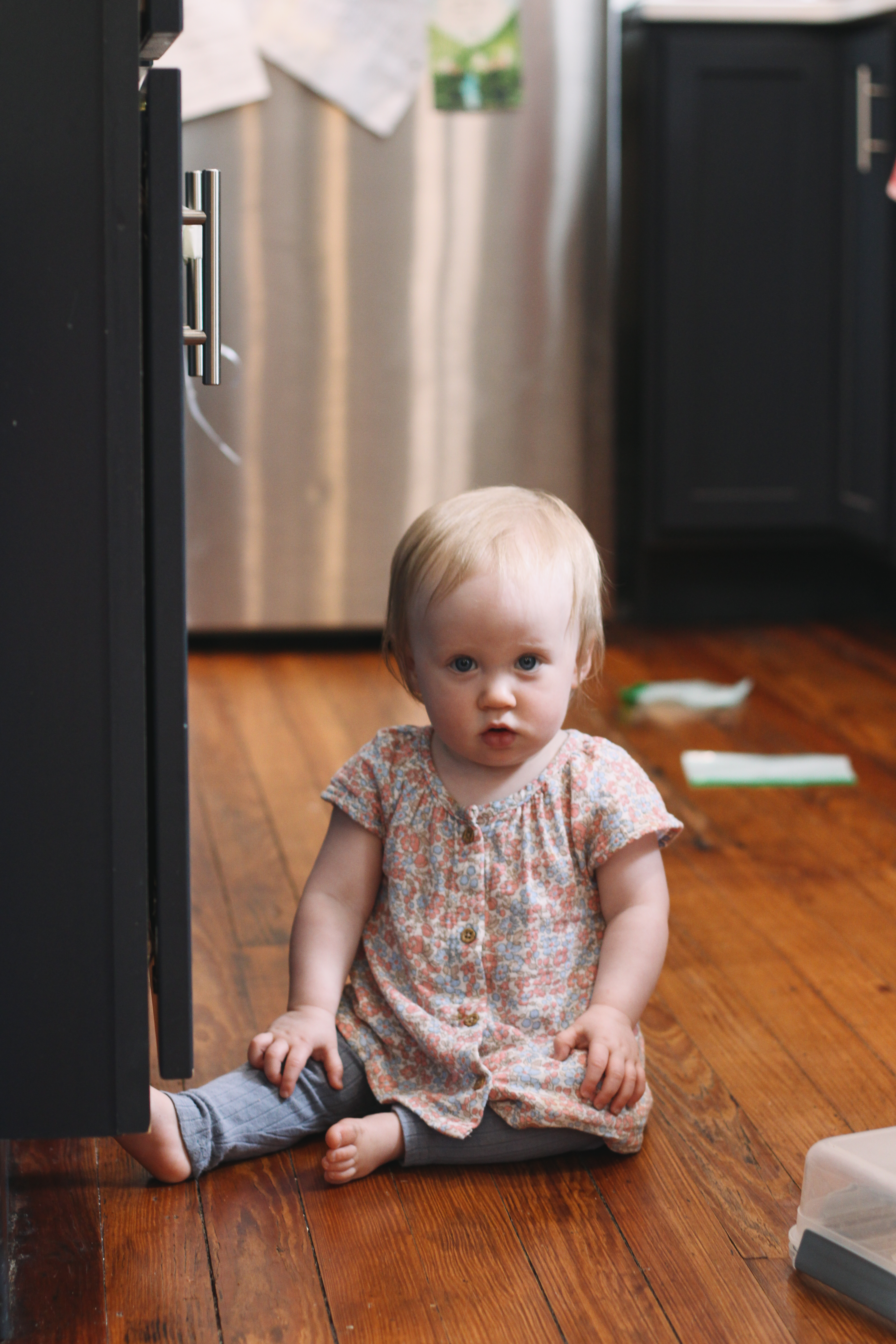A baby sitting on a hardwood kitchen floor next to dark cabinets